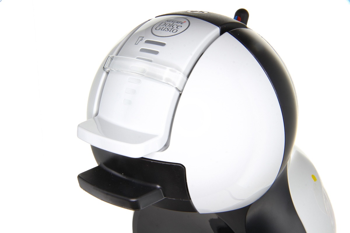 Nescafé Dolce Gusto kapselmaskin i arktiska grå/svarta färger, något upphöjd sidovy. Modern, rundad design med logotyp upptill. Kaffepip och droppbricka. Vit bakgrund.