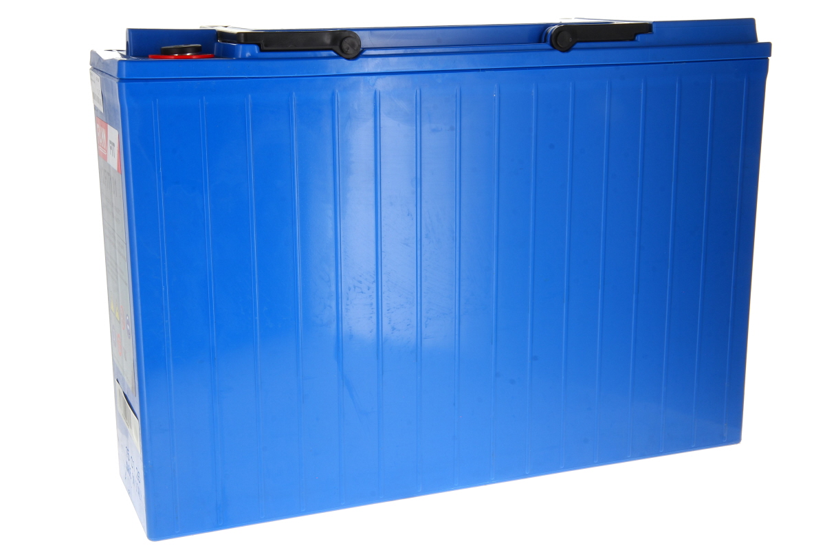 Large blue rectangular battery with vertical grooves on the sides. Black carrying handles at the top, a red cap and a black connector. Photographed on a white background, at a slight angle from the top right.