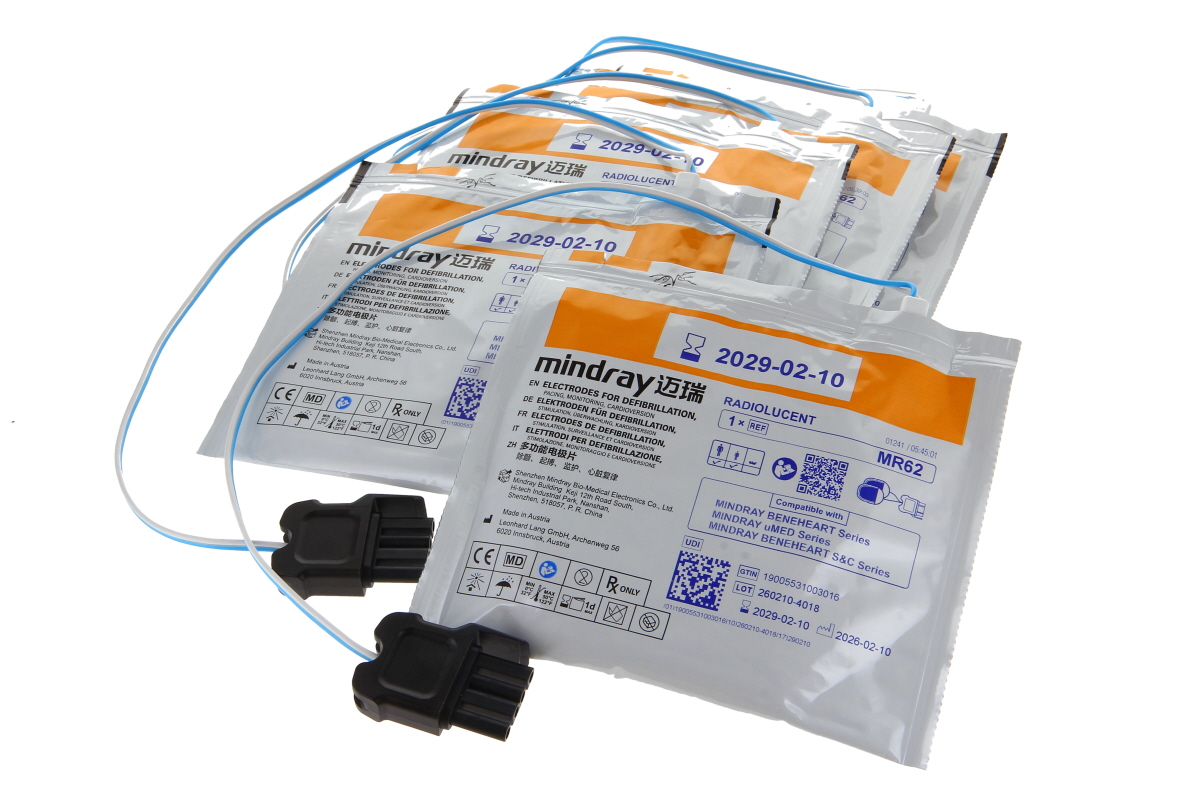Stapel weißer, einzeln versiegelter Mindray-Defibrillationselektroden-Packungen mit orange/blauen Akzenten und Aufdruck „ELECTRODES FOR DEFIBRILLATION“ in mehreren Sprachen. Blaue/weiße Kabel mit schwarzen Steckern. Haltbar bis 2029-02-10.