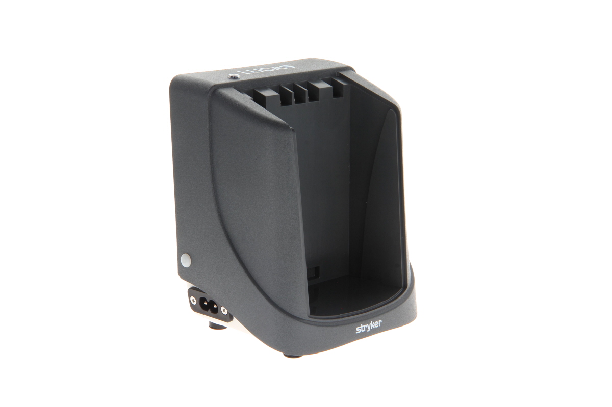 Dark grey, external charger for Lucas 2 and Lucas 3 medical devices. Features an open, vertical slot and is slightly wedge-shaped. ‘LUCAS’ is embossed on the top, with the power connection at the bottom.