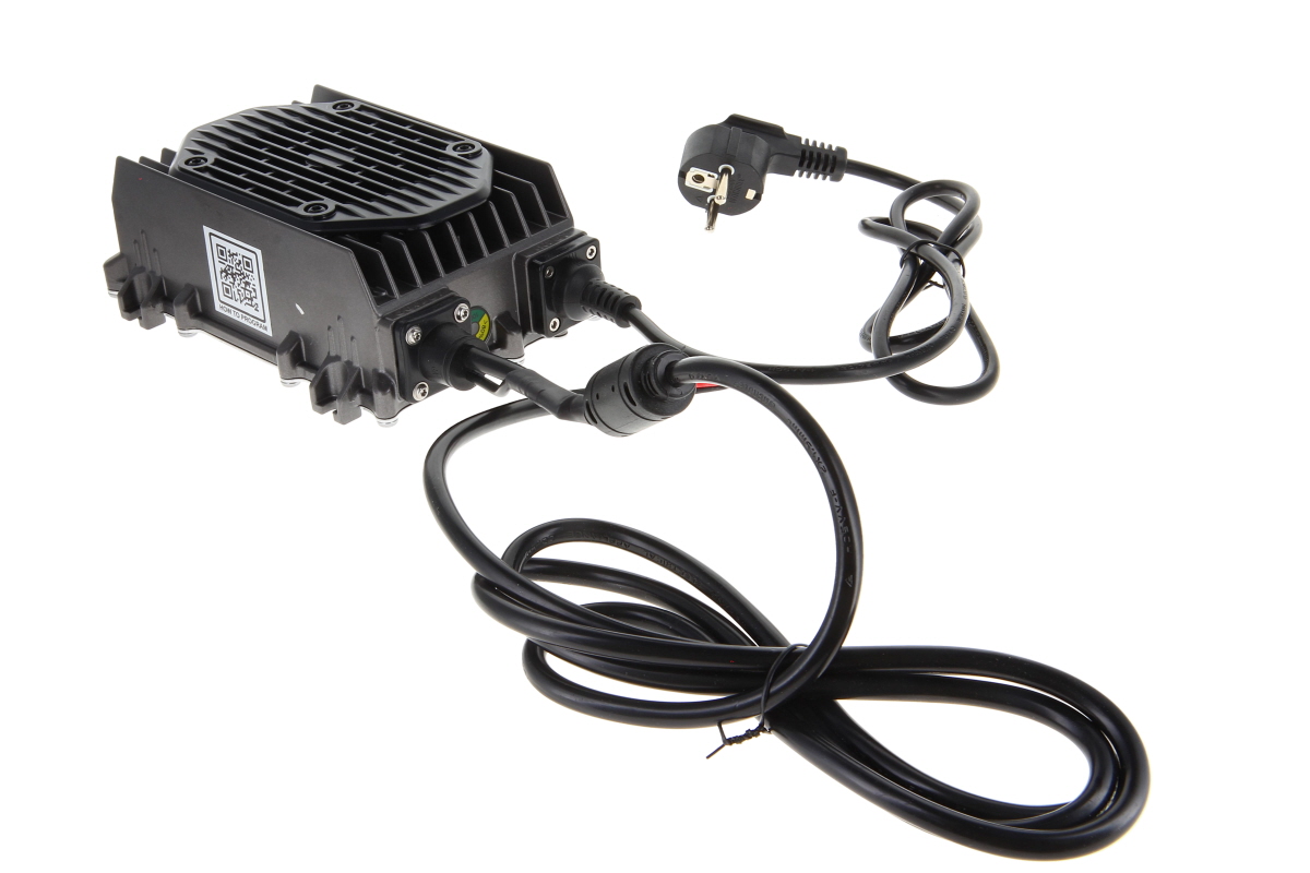 Schwarzes, rechteckiges Elektronikgerät mit gerippter Oberseite als Kühler. Seitlich gehen zwei schwarze Kabel ab, eines mit EU-Schuko-Stecker. Ein QR-Code mit "HOW TO PROGRAM" ist seitlich sichtbar. Kabel teils verdreht.