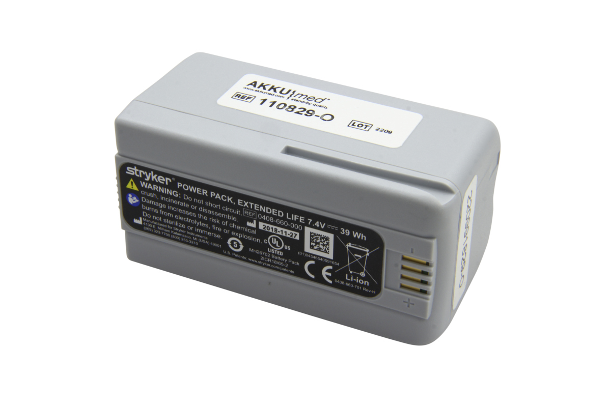 Batería de iones de litio gris «Stryker» para auriculares quirúrgicos, tipo 0408-660-000. Inscripción: 7,4 V, 39 Wh, Li-ion. Arriba, etiqueta «AKKUmed» con nº de referencia. Lateral: advertencias y 4 contactos dorados.