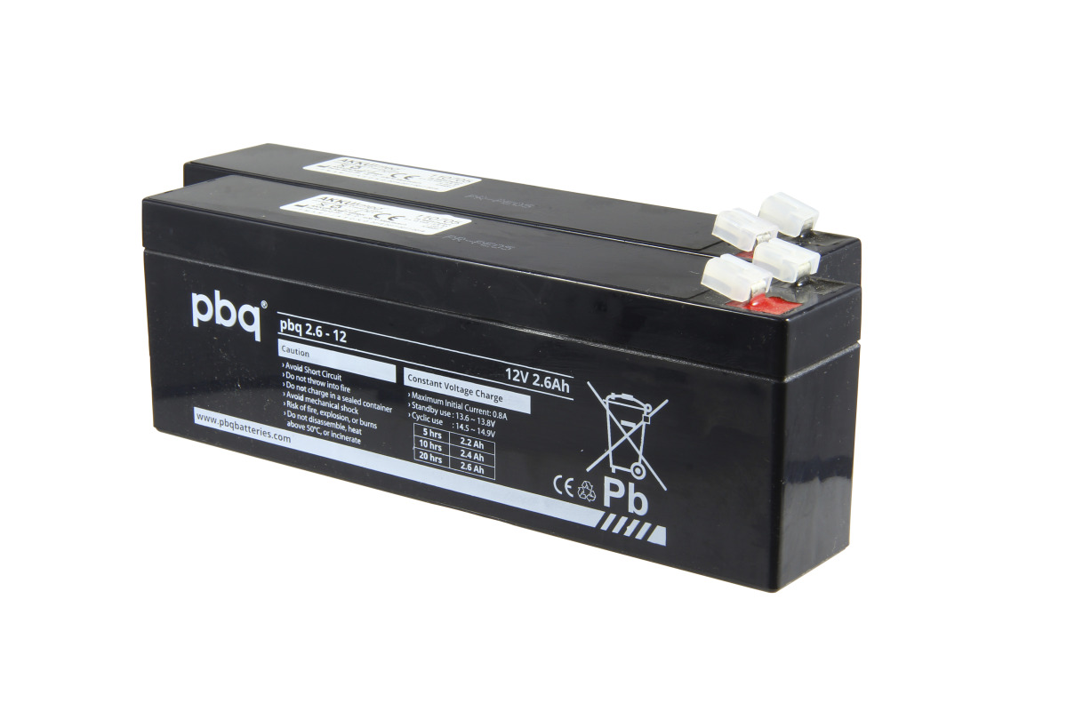 Two black, rectangular lead-acid batteries with white stickers reading ‘pbq 2.6 – 12’ and ‘12V 2.6Ah’. Warning labels and recycling symbols are visible. White plastic terminals on the top of each battery. Suitable for Liko ceiling lifts Hill Rom.
