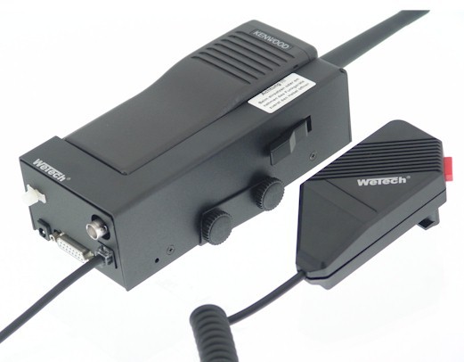Cargador para coche negro « Wetech » que sirve de soporte de carga para las radios « Kenwood » TK280/TK380 con micrófono de mano conectado. Con varias conexiones, incluida una toma SUB-D de 15 pines. Micrófono negro, con botón rojo.