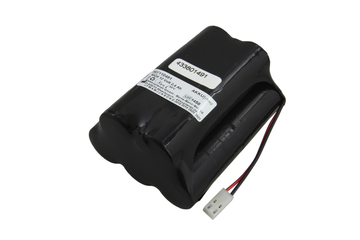 A black, cylindrical AKKUmed NC battery comprising several cells, lying at an angle on a white background. White label: ‘NICd 12 Volt 2.4 Ah’ etc. A red and black cable with a white plug is visible. Suitable for Atmos Atmoport N suction pumps.