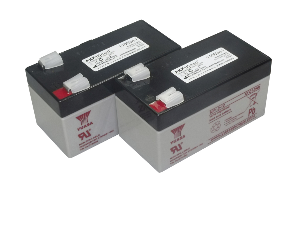 Two compact, grey lead-acid batteries with black covers, exposed terminals and white protective caps. Labelling: ‘AKKUmed ’, type ‘NP1.2-12’, ‘12V 1.2Ah’. For use as replacement battery packs, e.g. for hospital beds.