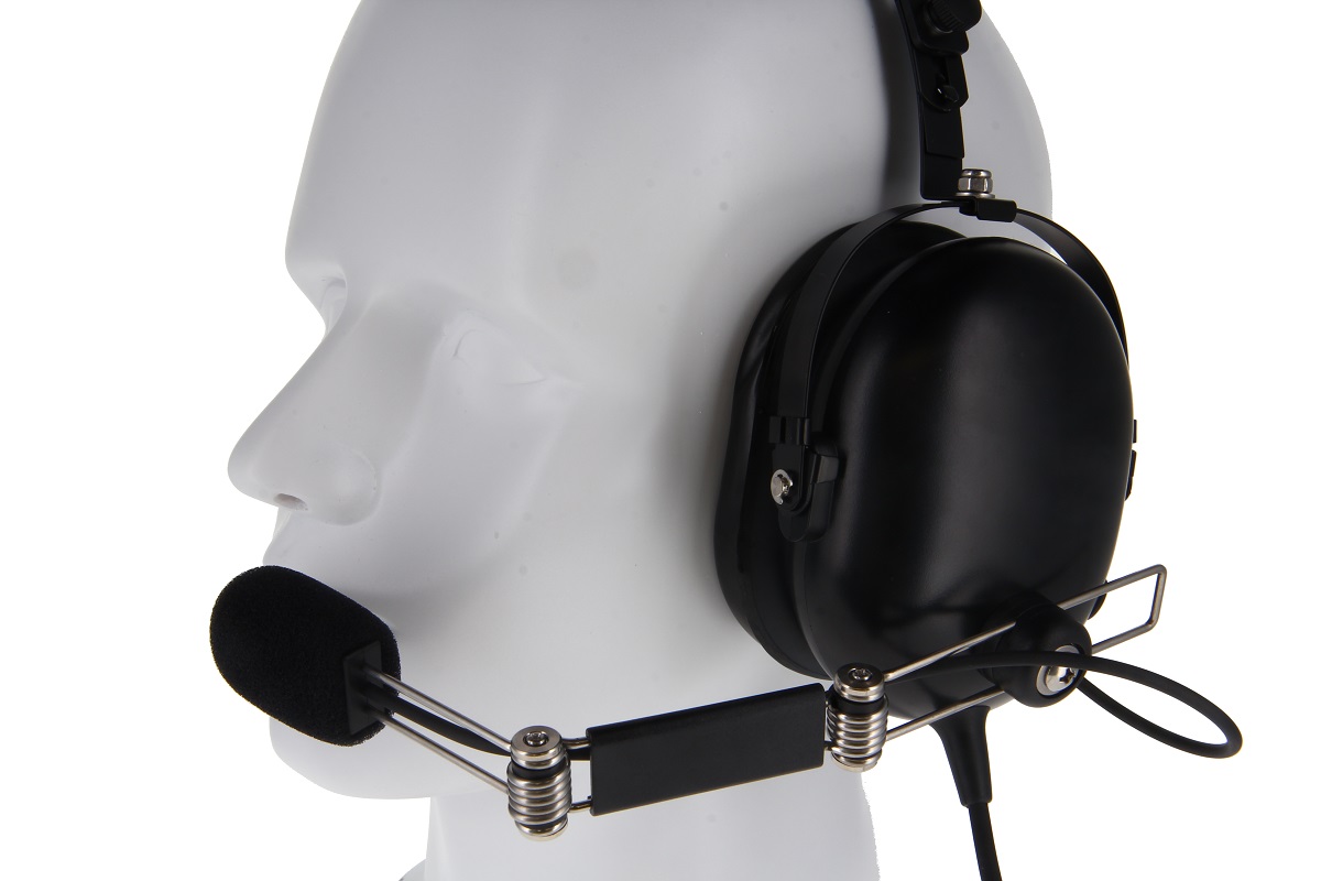 Auriculares monaurales negros « CoPacks » en una cabeza de maniquí blanca, de perfil. Gran auricular en la oreja derecha, micrófono flexible con espuma ante la boca. Resortes metálicos visibles. Para comunicación profesional.