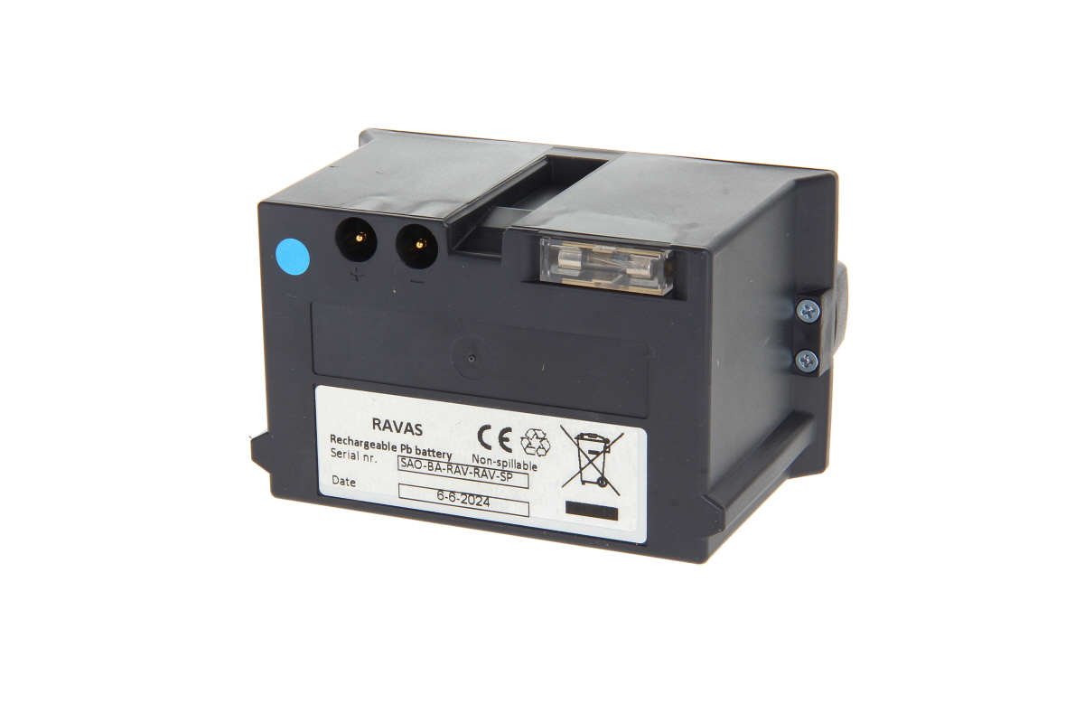 Black, rectangular Ravas lead-acid battery with two gold terminals and a blue dot on top. The transparent cover reveals a fuse. White front label: ‘Rechargeable Pb battery’ by RAVAS with the CE mark.