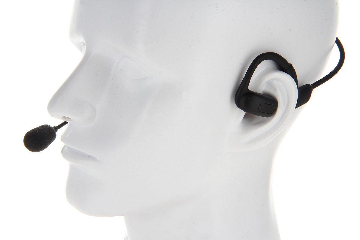 Schwarzes Open-Ear Headset an weißem Schaufensterpuppenkopf. Mit Ohrhaken und flexiblem Schwanenhalsmikrofon vor dem Mund für klare Kommunikation. Das Design erhält Situationsbewusstsein, da Umgebungsgeräusche hörbar bleiben.