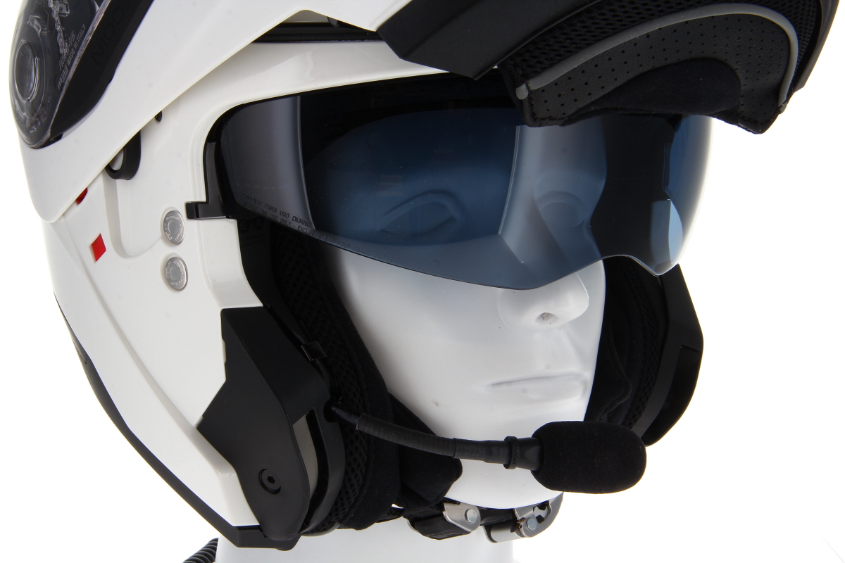 Weißer Nolan N100-6 Klapphelm auf weißem Schaufensterpuppenkopf von der Seite. Der Helm hat ein heruntergeklapptes dunkles Sonnenvisier. Schwarzes TITAN Helmsprechsystem mit Schaumstoffmikrofon links am Mundbereich.
