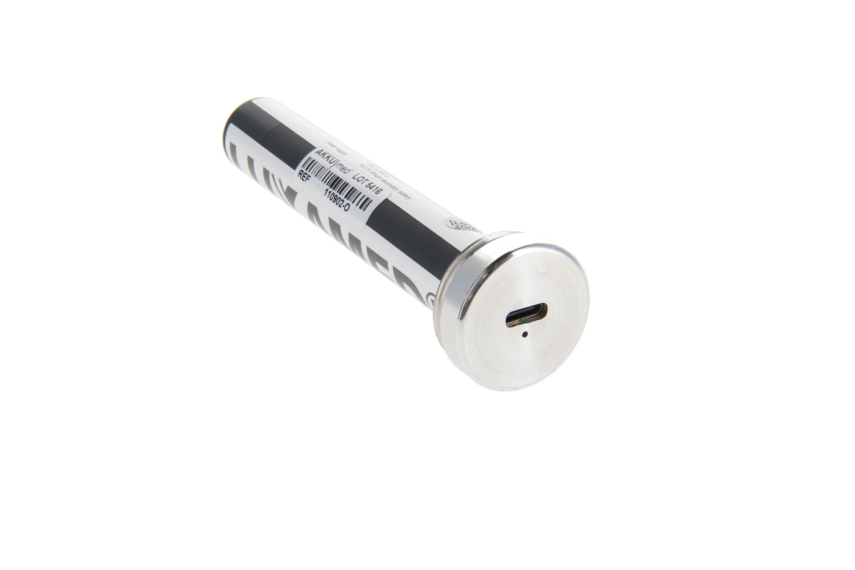 Módulo de carga cilíndrico plateado «Luxamed» con rotulación negra y código de barras. Un extremo tiene tapa metálica brillante, conector USB-C y pequeño LED. Incluye batería de iones de litio para uso médico.